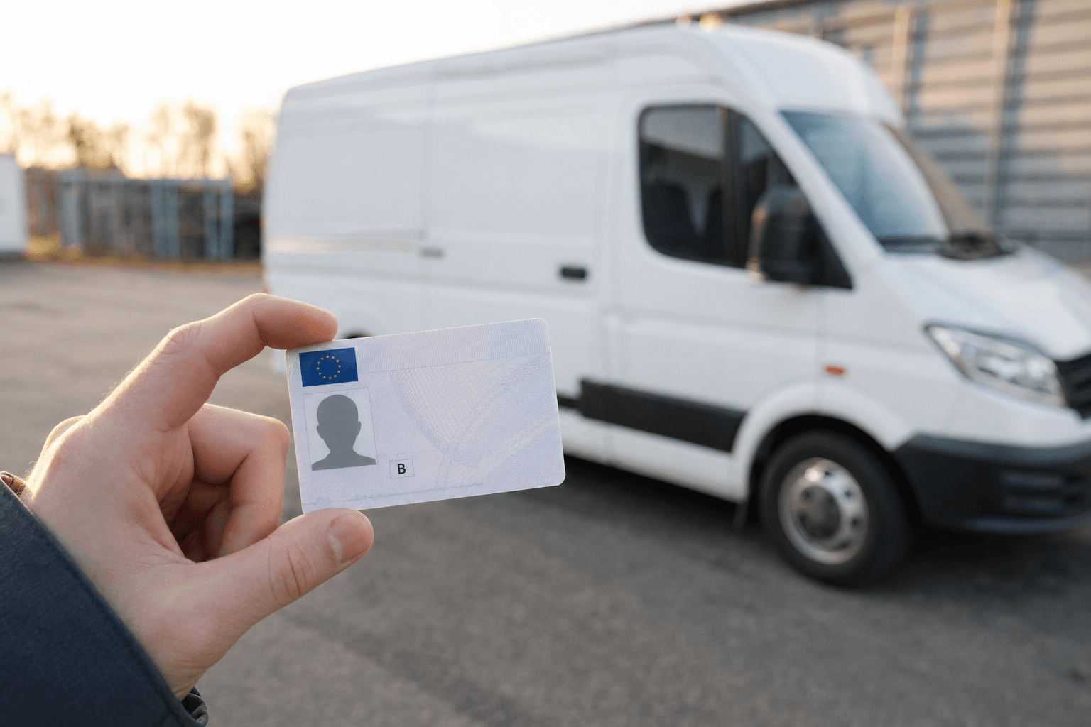Ruka držící český řidičský průkaz skupiny B před zaparkovanou bílou dodávkou